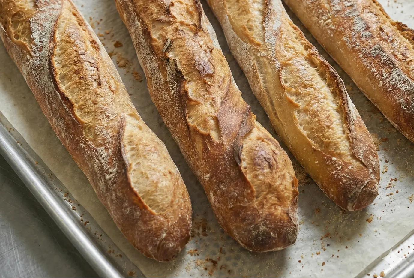 Baguettes tradition françaises tout juste sorties du four, disposées sur une plaque de cuisson, avec une croûte dorée et de belles grignes ouvertes.