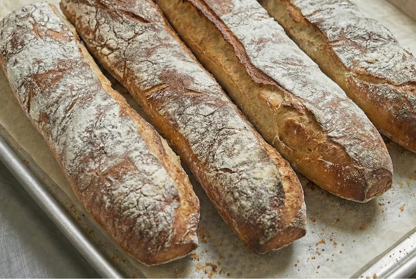 Pain rustique fraîchement cuit, disposé sur une plaque de cuisson. Les baguettes présentent une croûte dorée et farinée, avec des grignes bien ouvertes.