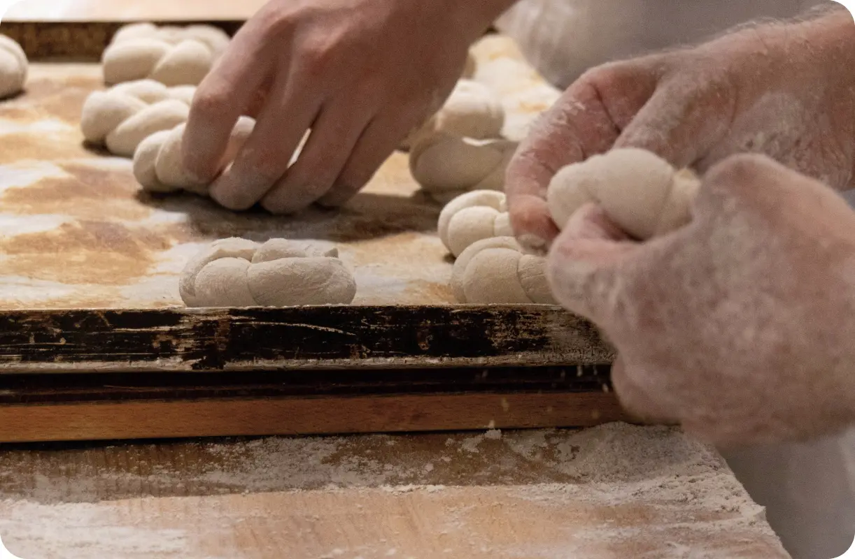 Mains de boulangers en train de tresser et façonner à la main de la pate sur un plan de travail fariné, dans un environnement de fabrication artisanale.