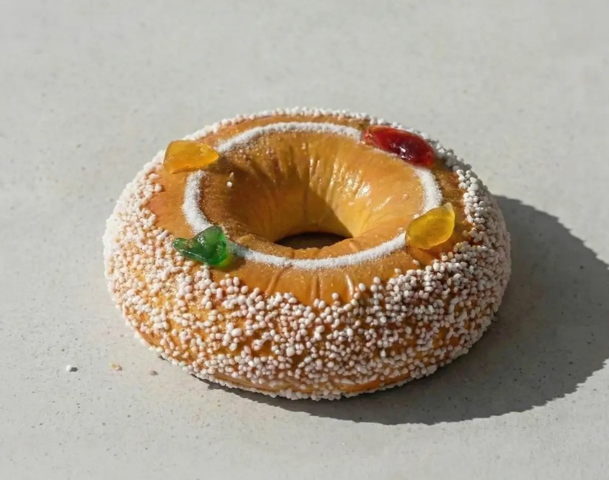Couronne briochée individuelle dorée, décorée de sucre perlé, de lignes de sucre glace et de petits bonbons gélifiés colorés, posée sur une surface claire et éclairée par la lumière naturelle.