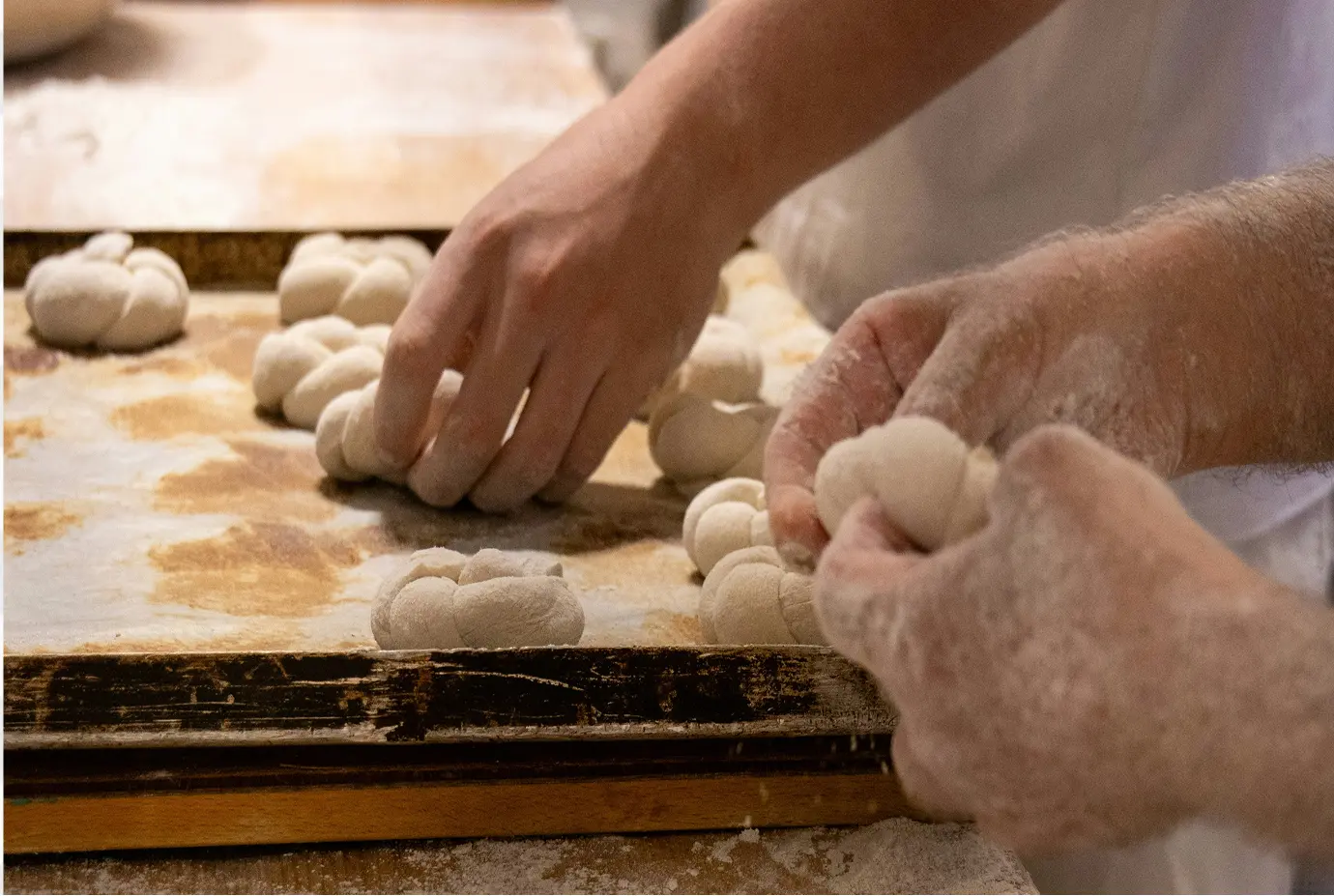 Mains de boulangers en train de tresser et façonner à la main de la pate sur un plan de travail fariné, dans un environnement de fabrication artisanale.