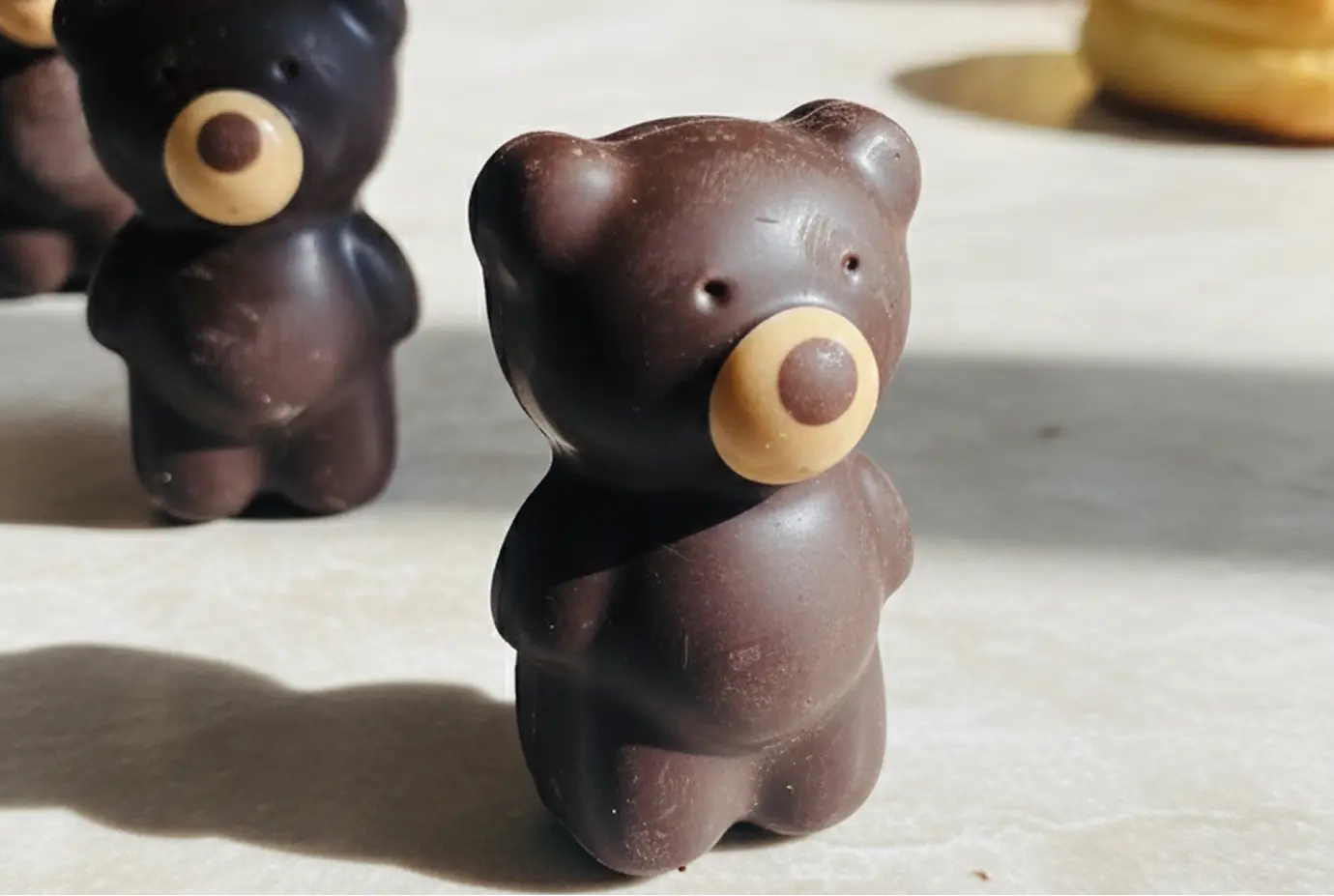 Ourson en chocolat noir avec un museau en chocolat blanc et au lait avec gimauve à l'intérieur, debout sur une surface claire et éclairé par la lumière naturelle.